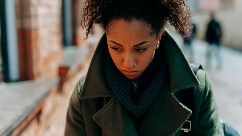 A woman in a green coat looking down with a worried expression