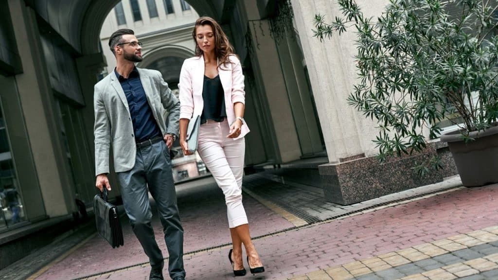 A man and woman in business suits walk together through an outdoor stone archway.