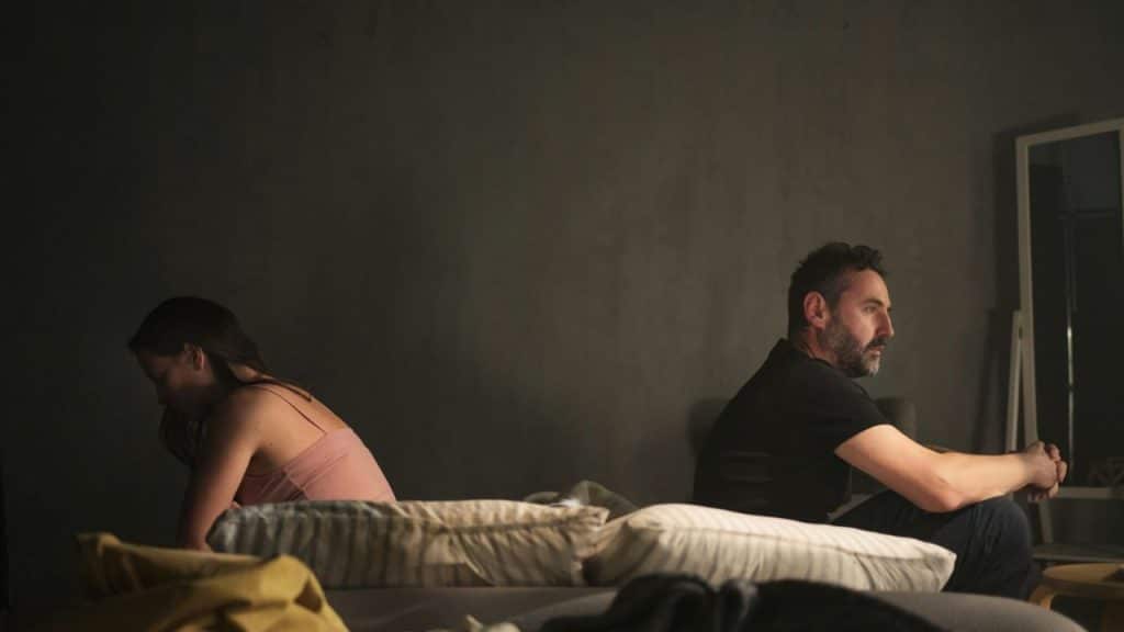 A man and woman sit on a bed with their backs to each other.