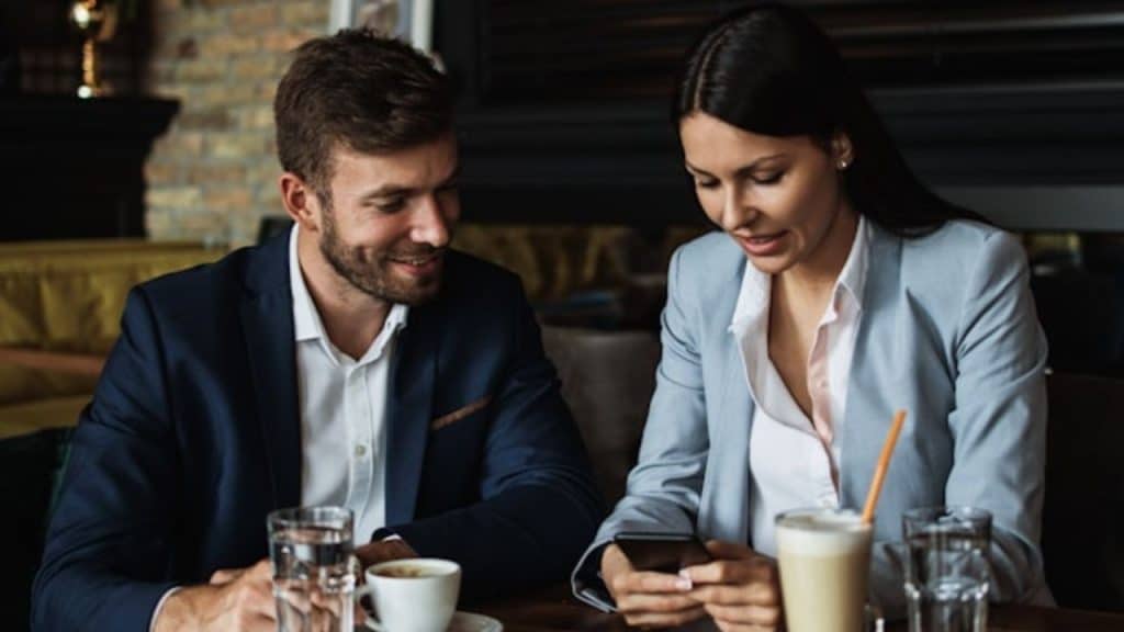 A man and woman in business attire sit at a table with coffee.