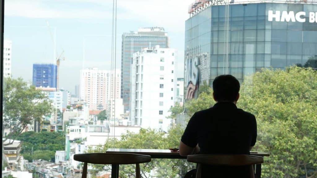 A man sitting alone at a table looking out at the city through a large window.