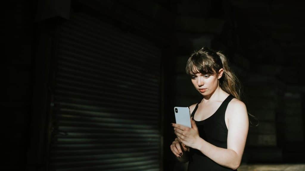 A woman in athletic wear looks at her phone in a dark outdoor setting.