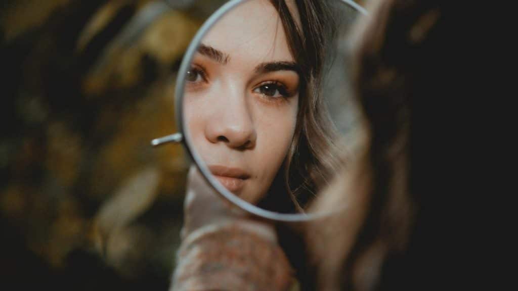 A person’s face reflected in a small handheld mirror.