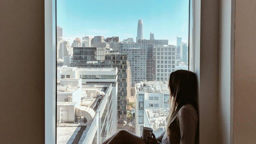 A person sitting by a window holding a mug and looking out over a city skyline.