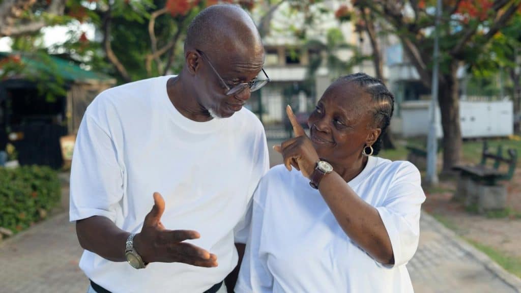 An older couple in white shirts smiling and talking together outdoors.