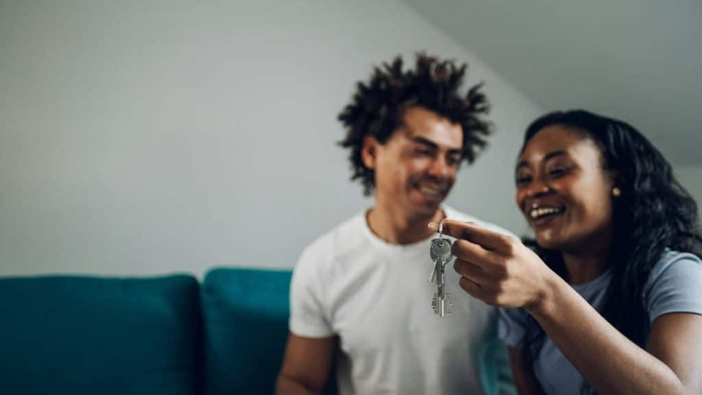 A smiling couple holding up a set of keys in a living room.