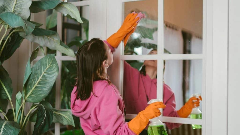 A woman wearing gloves while cleaning a window with a spray bottle.