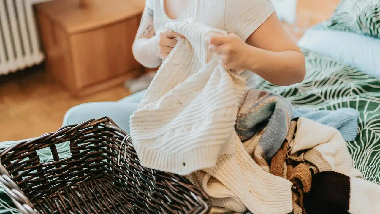 A person folding clothes from a laundry basket on a bed.