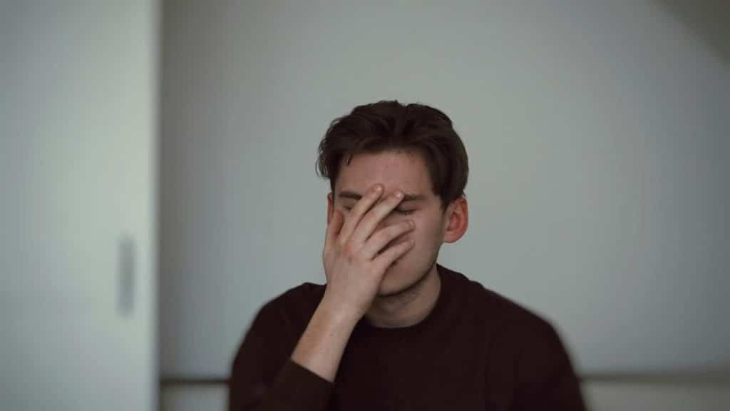 A man covering his face with one hand against a plain background.