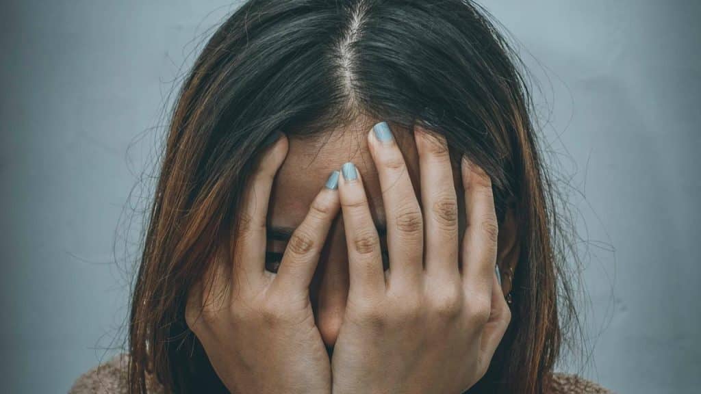 A person covering their face with both hands against a plain background.
