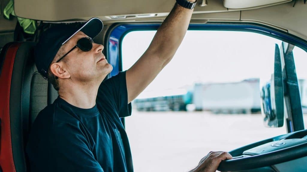 A man wearing sunglasses adjusting controls inside a truck cab
