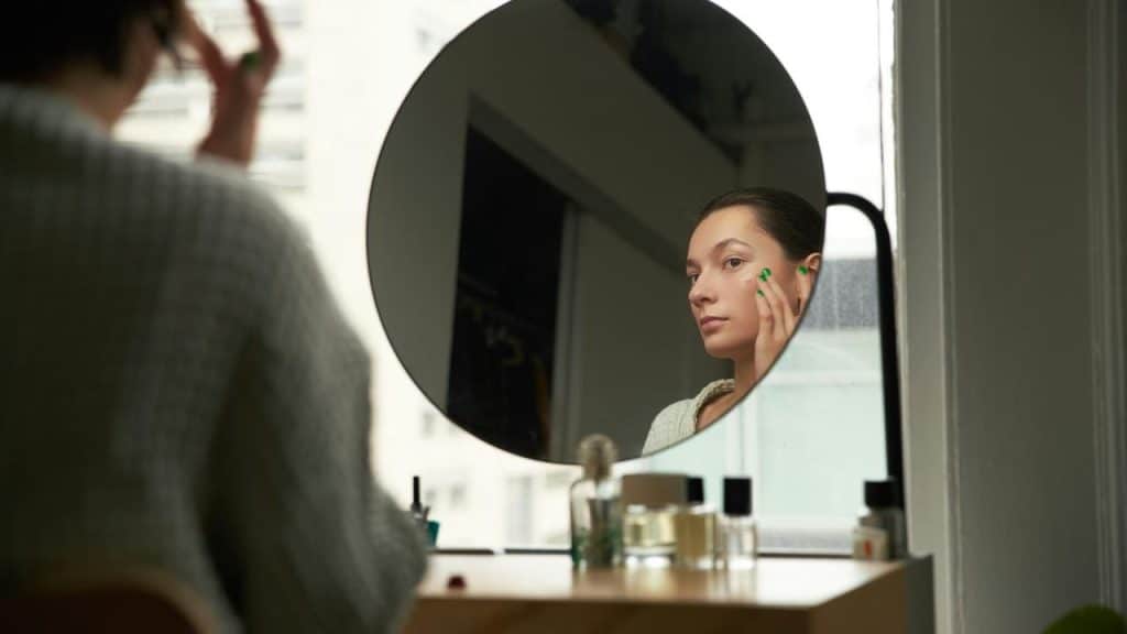 A woman touching her face while looking at herself in a round mirror.