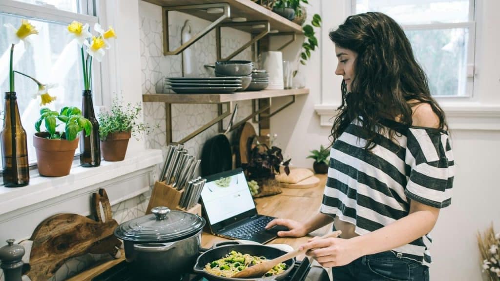 A woman cooking at a stove while following a recipe on a laptop.