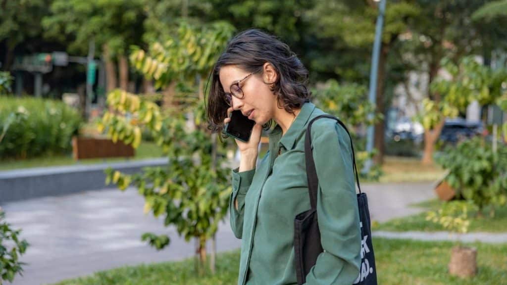 A woman talking on a phone while walking through a green park.