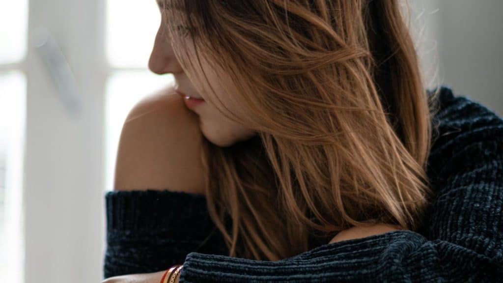 A woman with long hair looking down thoughtfully by a window.