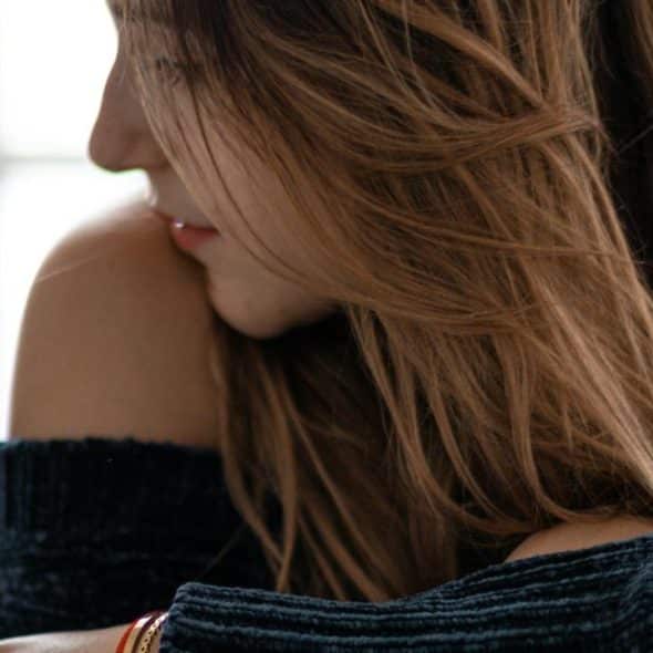 A woman with long hair looking down thoughtfully by a window.