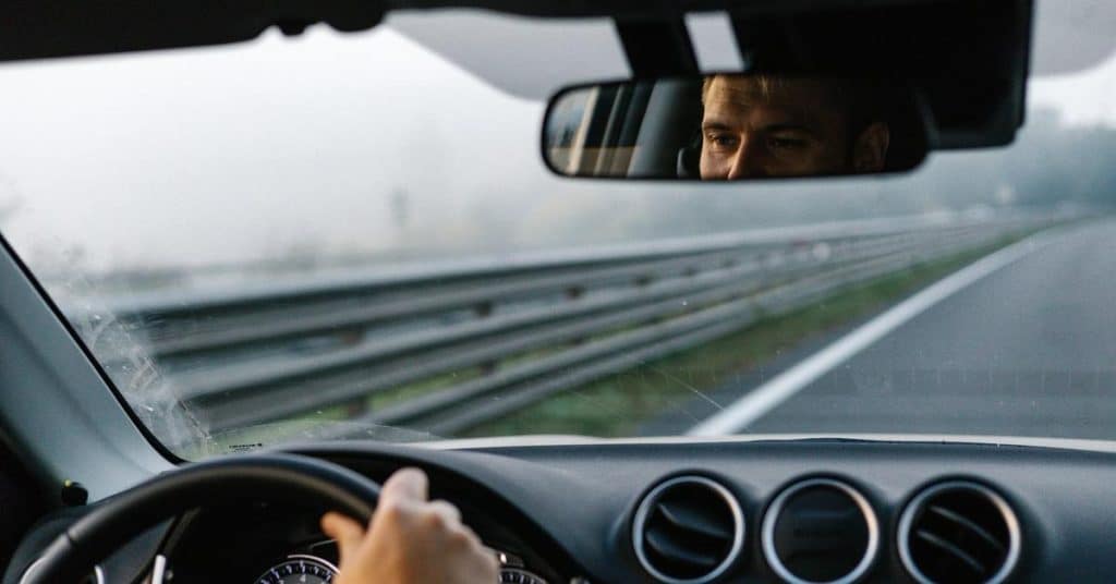 A driver grips the steering wheel while driving on a foggy road.