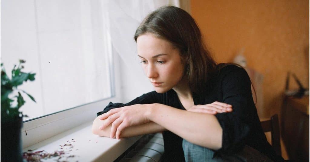 A person leans on a windowsill and gazes outside thoughtfully.