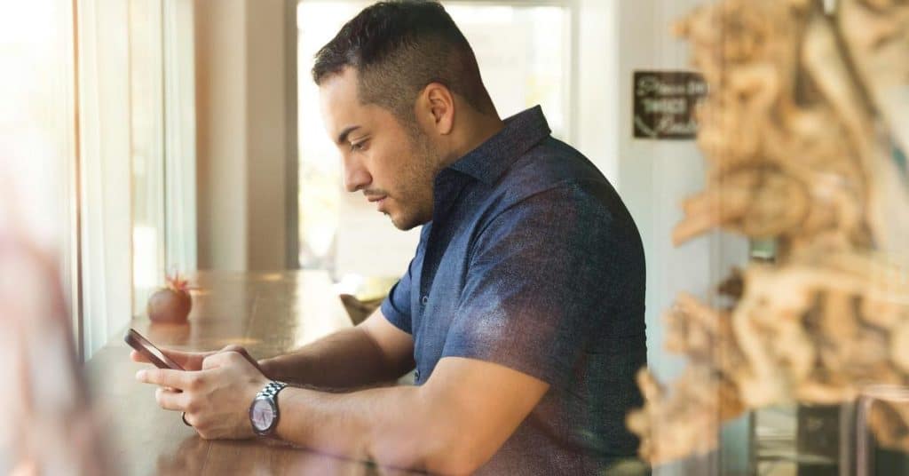 A man sits at a table and looks at his phone.