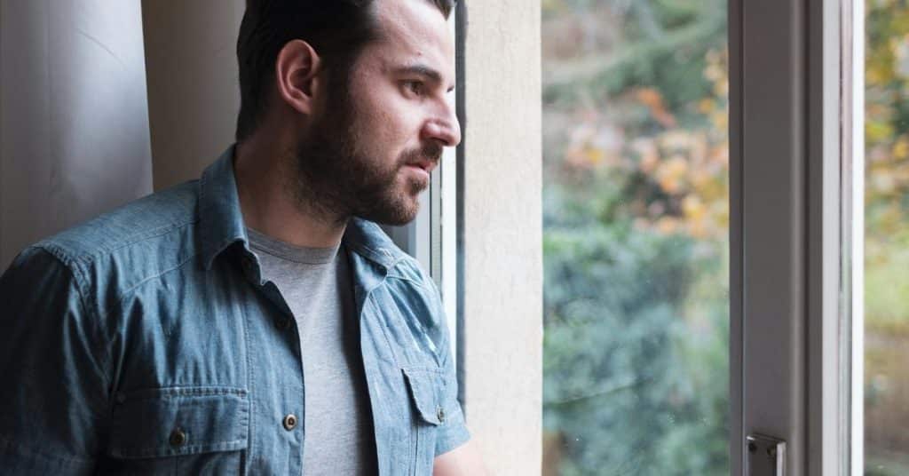A man stands by a window looking outside thoughtfully.