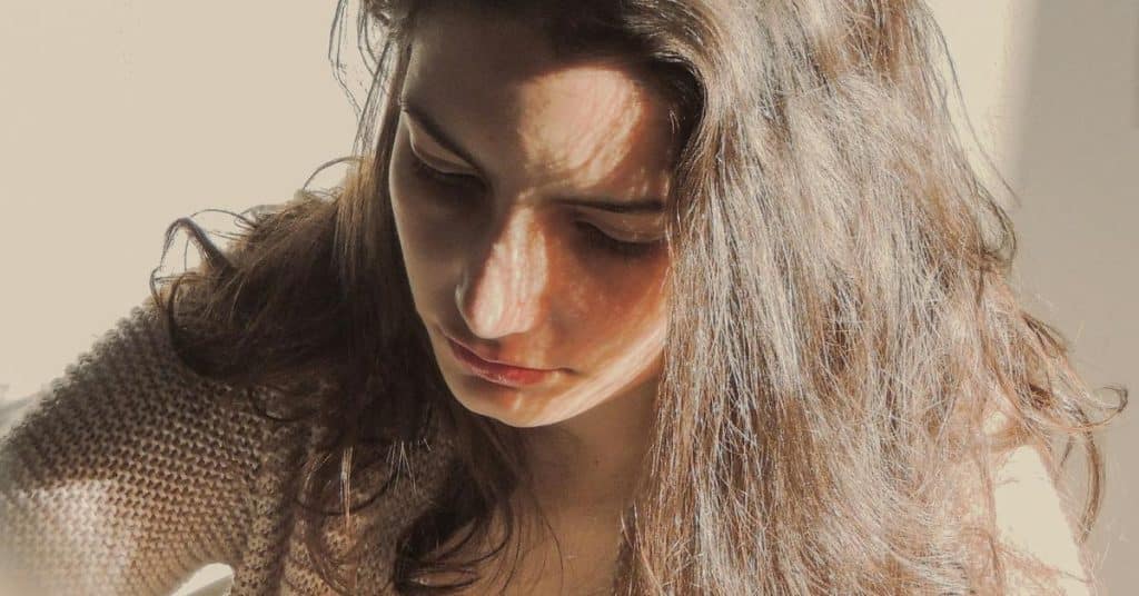 A person looks downward as sunlight falls across their face and hair.
