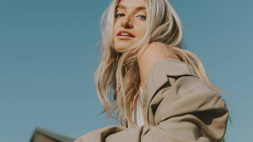 A woman with long blonde hair posing outdoors under a clear blue sky.
