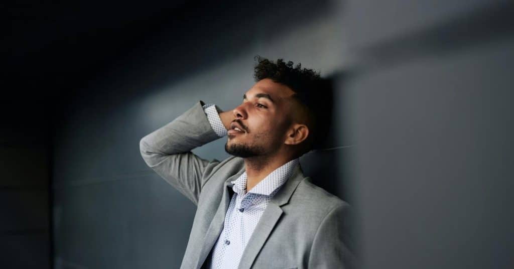 A man leaning against a wall with his hand on his head, looking thoughtful.