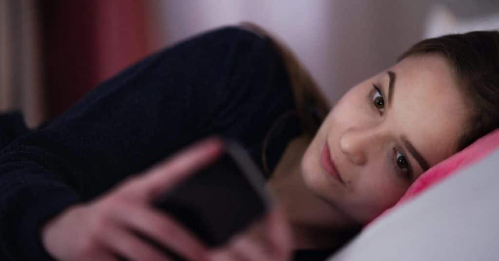 A woman lying on a pillow, looking at her phone.