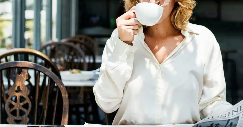 A woman sipping coffee while reading a newspaper at a café.