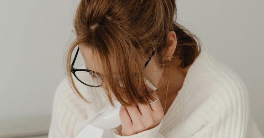 A woman wearing glasses looking down with her hand near her face.