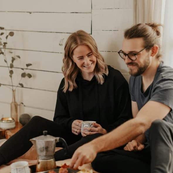 A couple sitting on a bed sharing coffee