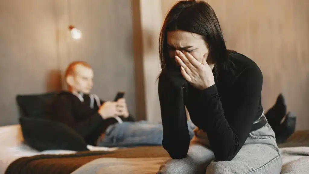 A distressed woman covering her face while another person sits in the background.