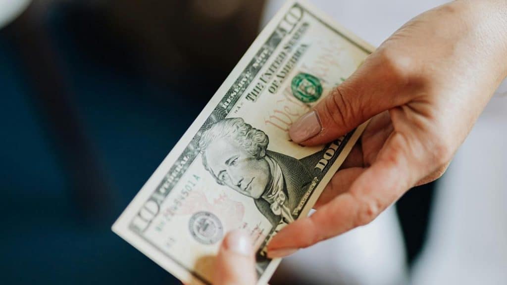 A hand giving another person a twenty-dollar bill.