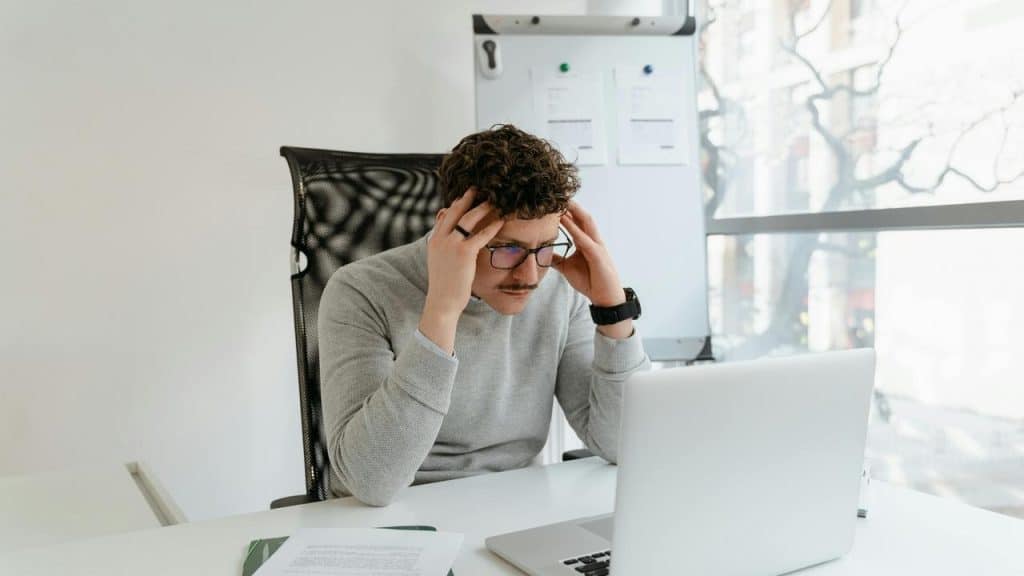 A man looking stressed while working on a laptop.