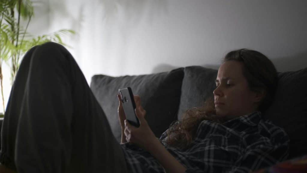 A woman lying on a couch looking at her phone.