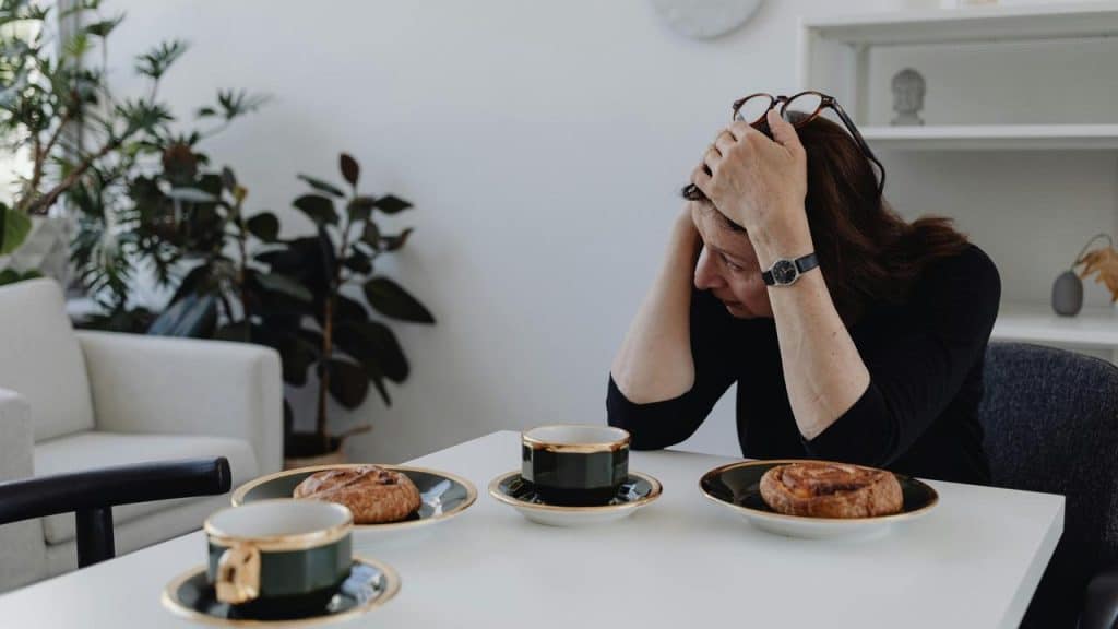 A woman sitting at a table looking stressed with coffee and pastries.