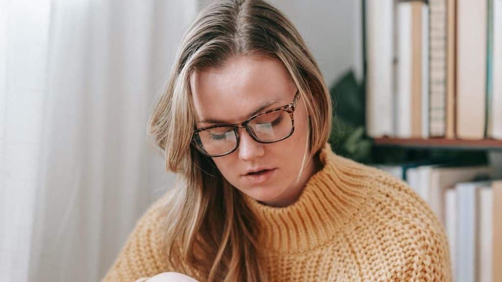 A woman wearing glasses looking down while reading indoors.