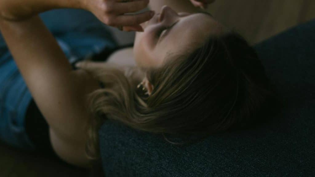 A woman lying on a couch looking at a phone in dim lighting.