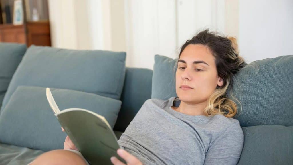 A woman lying on a couch reading a book.