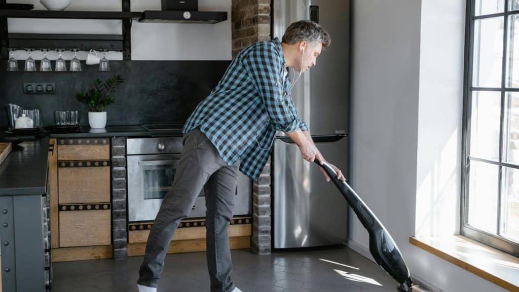 A man vacuuming the floor in a modern kitchen.