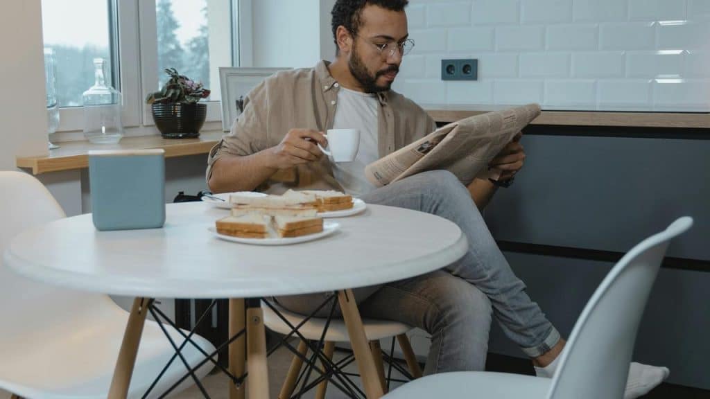 A man sitting at a table reading a newspaper while holding a cup.