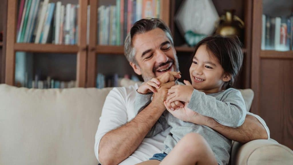 A man sitting on a couch playfully holding a smiling child.