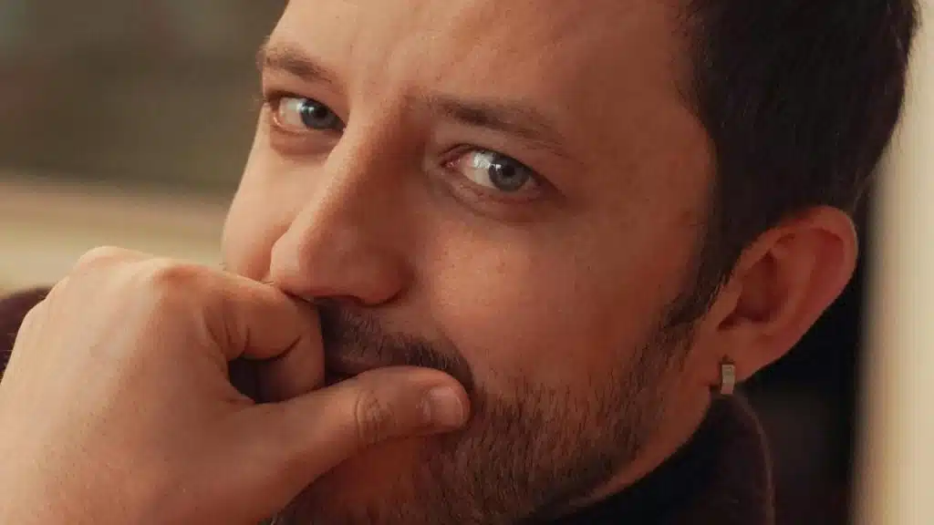 A man rests his hand near his mouth while looking thoughtful.