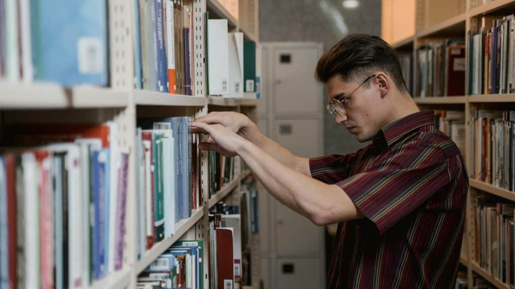 A man searches for a book on a library shelf.