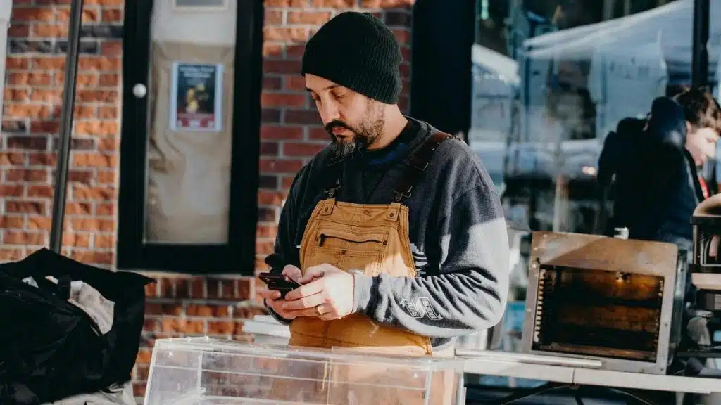 A man wearing an apron checks his phone while working.