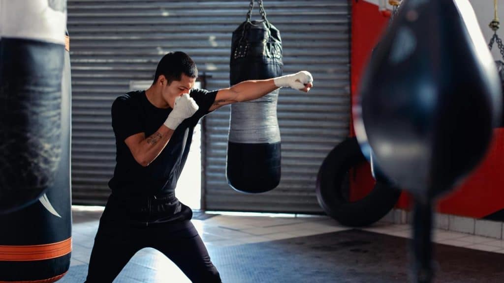 A man practices boxing with a punching bag in a gym.
