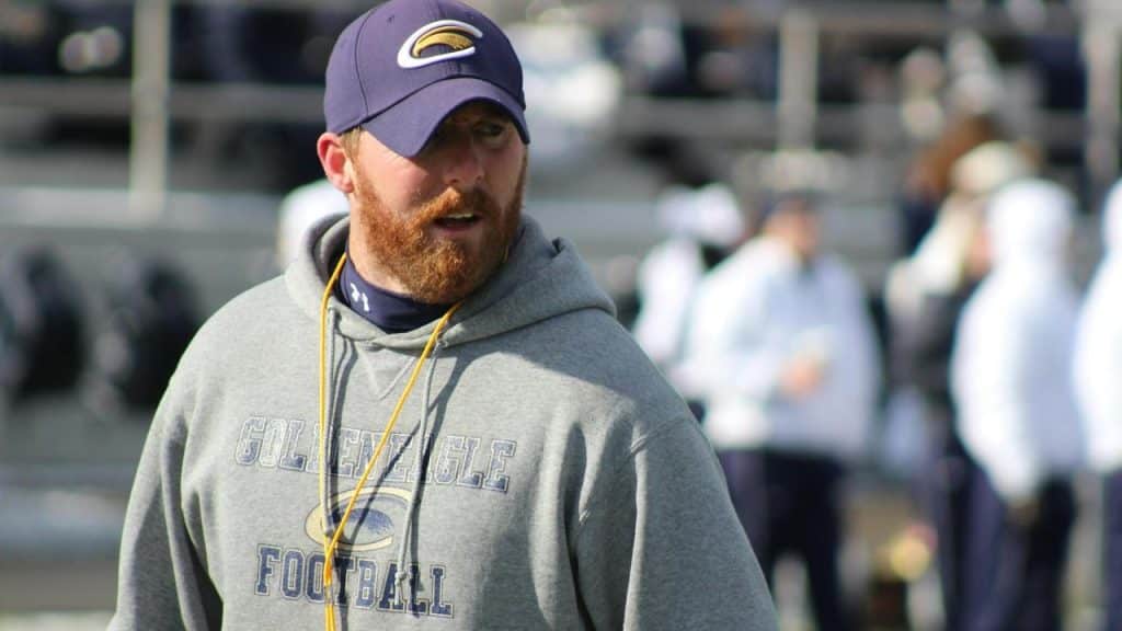 A football coach stands on a field during practice.