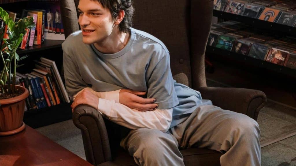 A man sits in a chair smiling while talking indoors.