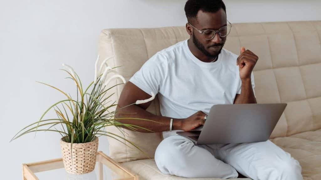 A man wearing glasses uses a laptop while sitting on a couch.