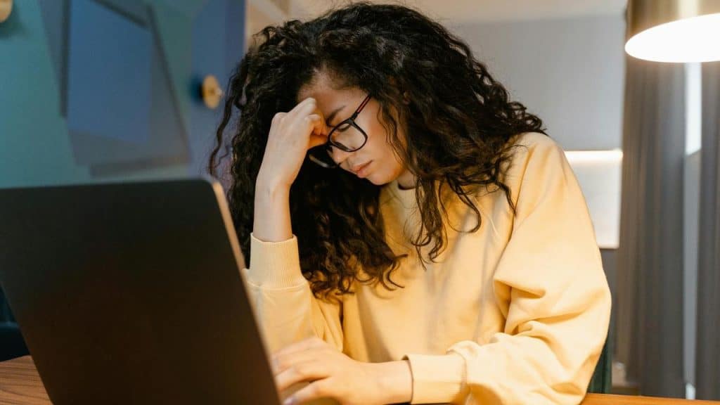 A woman wearing glasses looks stressed while working on a laptop.